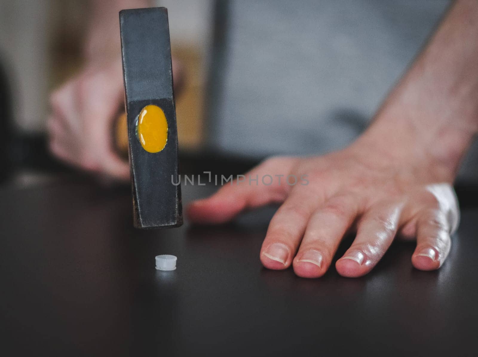 Caucasian young unrecognizable man hammers a white plastic dowel into a black table shelf using a hammer while sitting on the floor in a room, close-up side view with depth of field. Furniture assembly concept, assembly services.