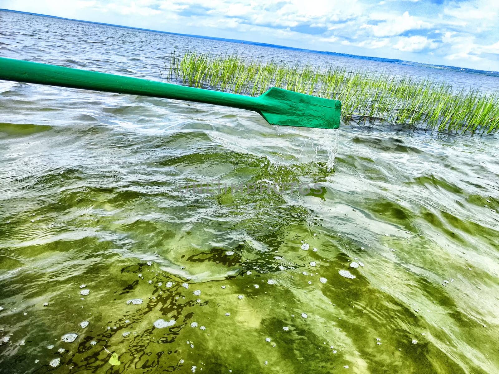 The paddle of a boat and the water of a large lake in the background. Natural landscape, travel, recreation. boat paddle extends over a calm lake