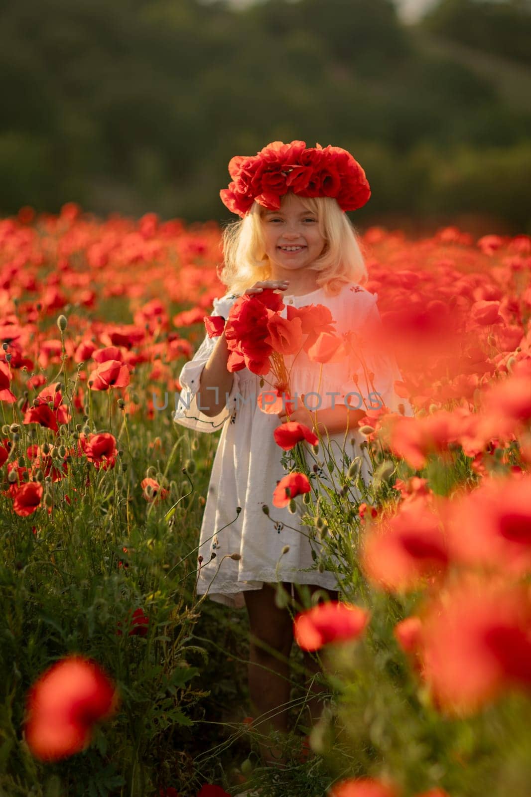 A young girl is standing in a field of red poppies. She is wearing a red headband and a white dress. by Matiunina