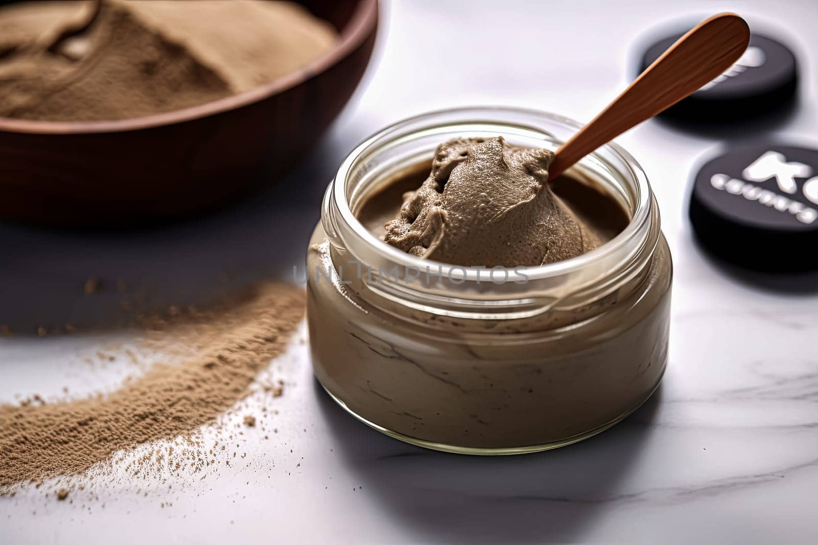 A jar of green facial clay sits on the table next to a bowl and spoon. The jar is filled with a caring face mask