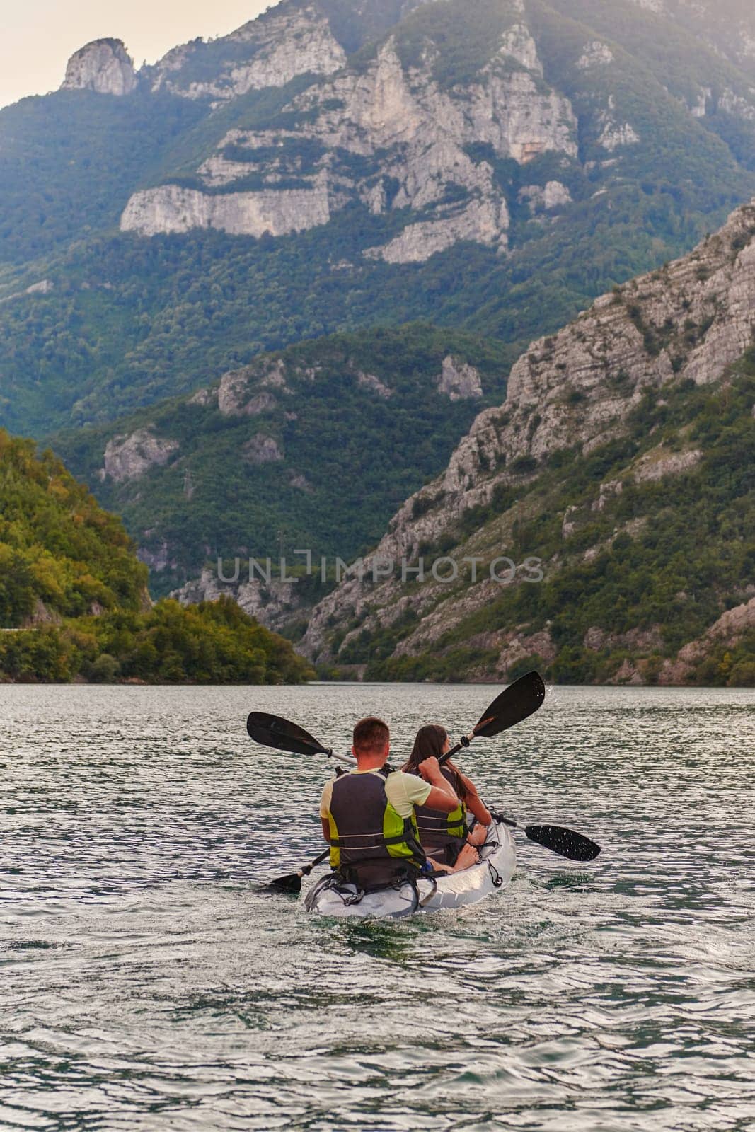 A young couple enjoying an idyllic kayak ride in the middle of a beautiful river surrounded by forest greenery in sunset time by dotshock