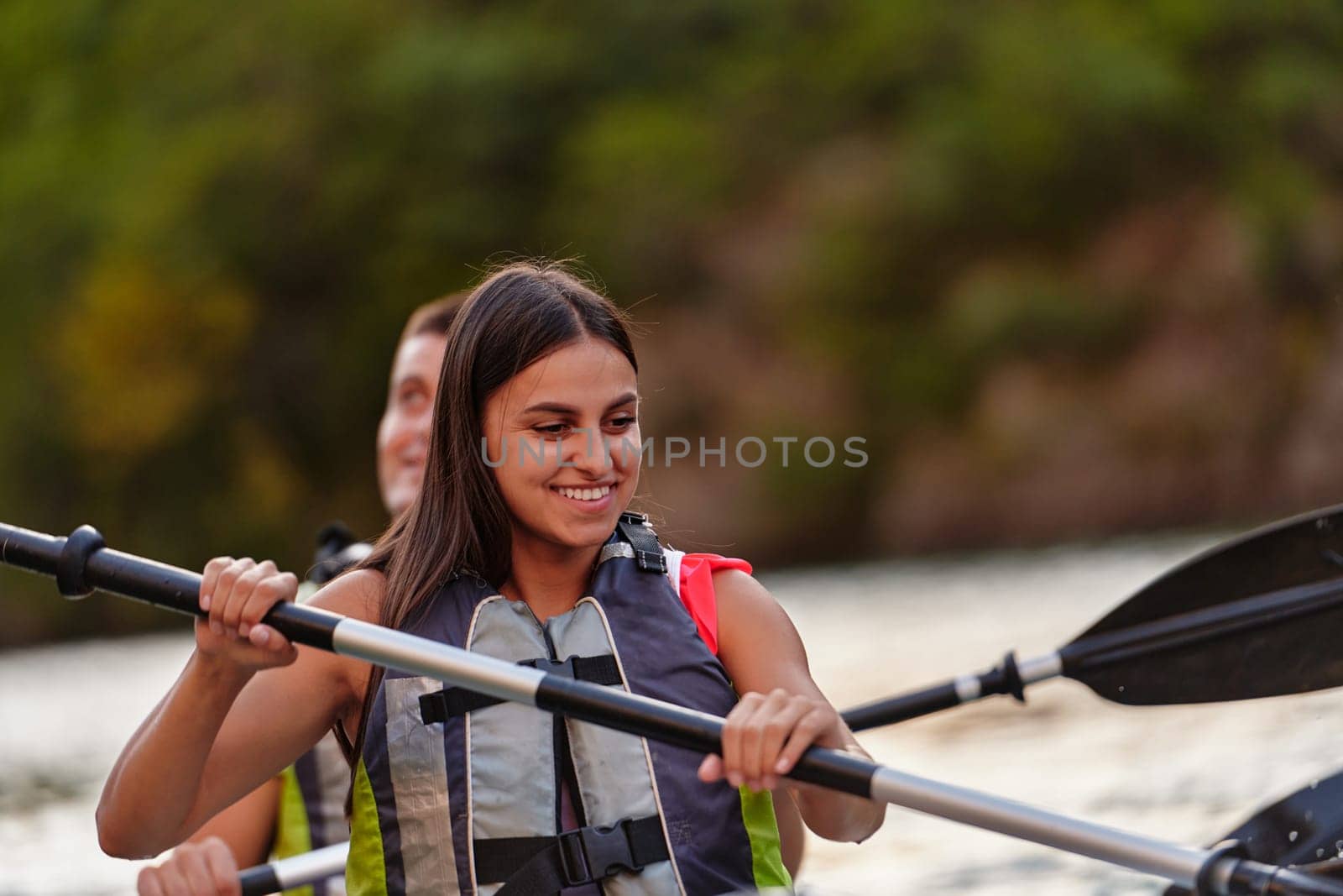 A young couple enjoying an idyllic kayak ride in the middle of a beautiful river surrounded by forest greenery.