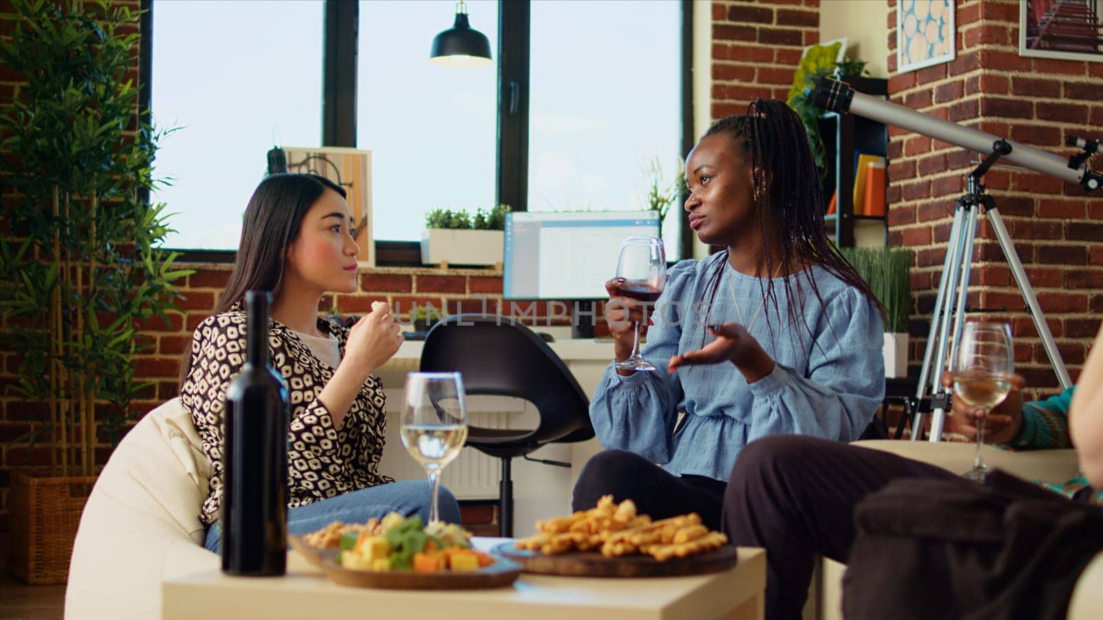 Multiracial women at brunch gathering trying out gourmet cheese from charcuterie board, smelling and tasting it. Curious BIPOC friends in stylish apartment sampling delicacies