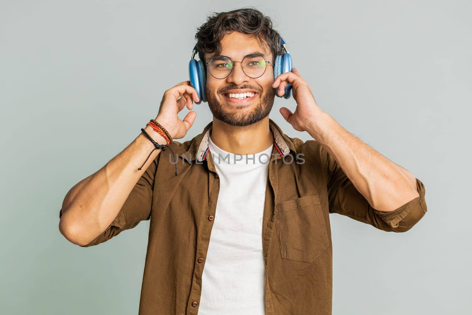 Happy smiling man listening music in headphones dancing disco fooling around having fun expressive gesticulating hands relaxing chill making funny moves. Indian bearded guy isolated on gray background