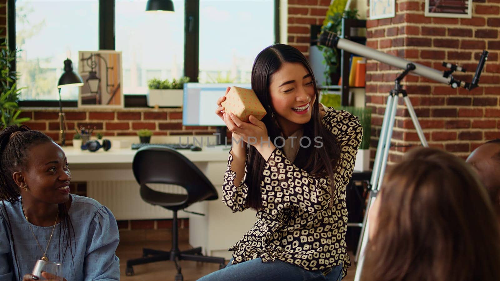 Multiethnic friends throwing surprise birthday party for asian woman, giving her thoughtful gift. Happy group of people celebrating host anniversary, gifting her small present