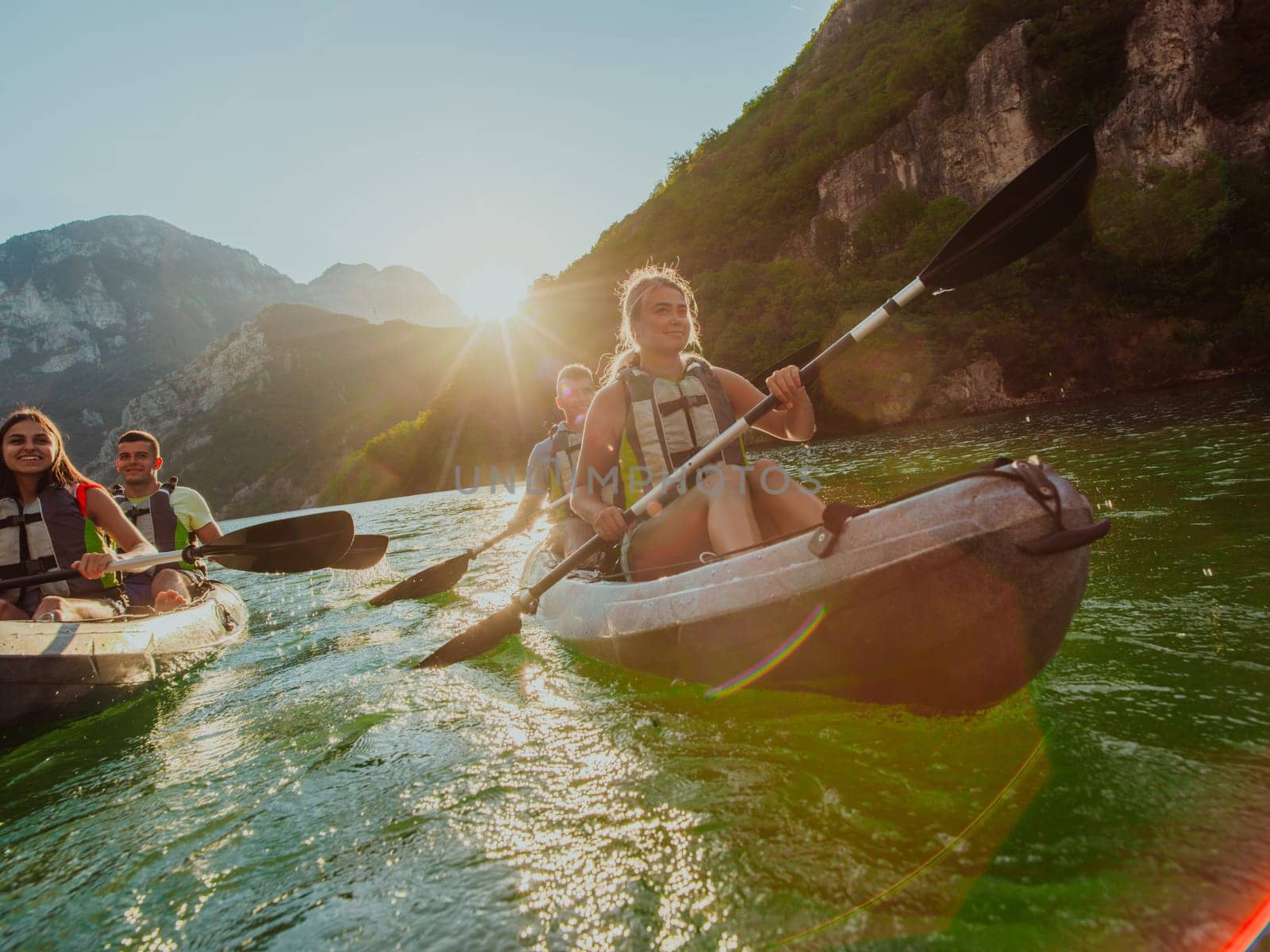 A group of friends enjoying fun and kayaking exploring the calm river, surrounding forest and large natural river canyons during an idyllic sunset