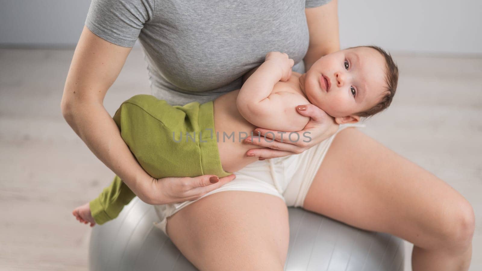 A faceless woman rocks her newborn son on a fitball