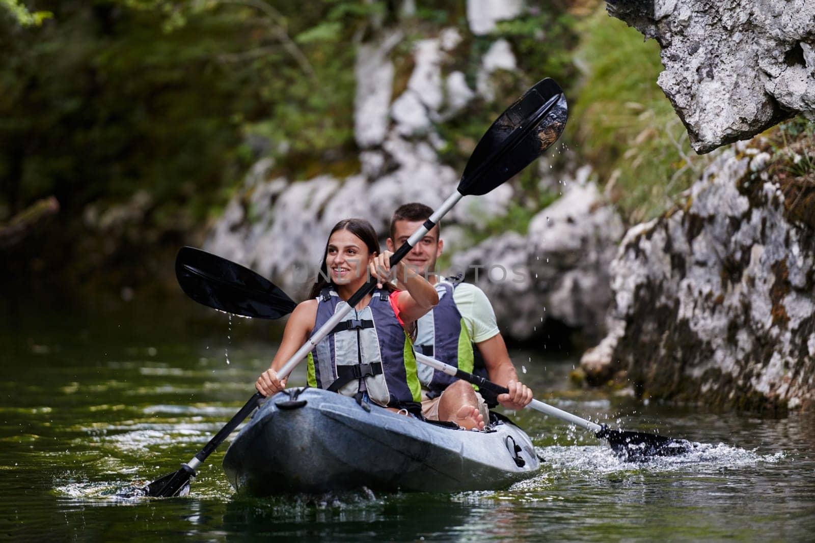 A young couple enjoying an idyllic kayak ride in the middle of a beautiful river surrounded by forest greenery.