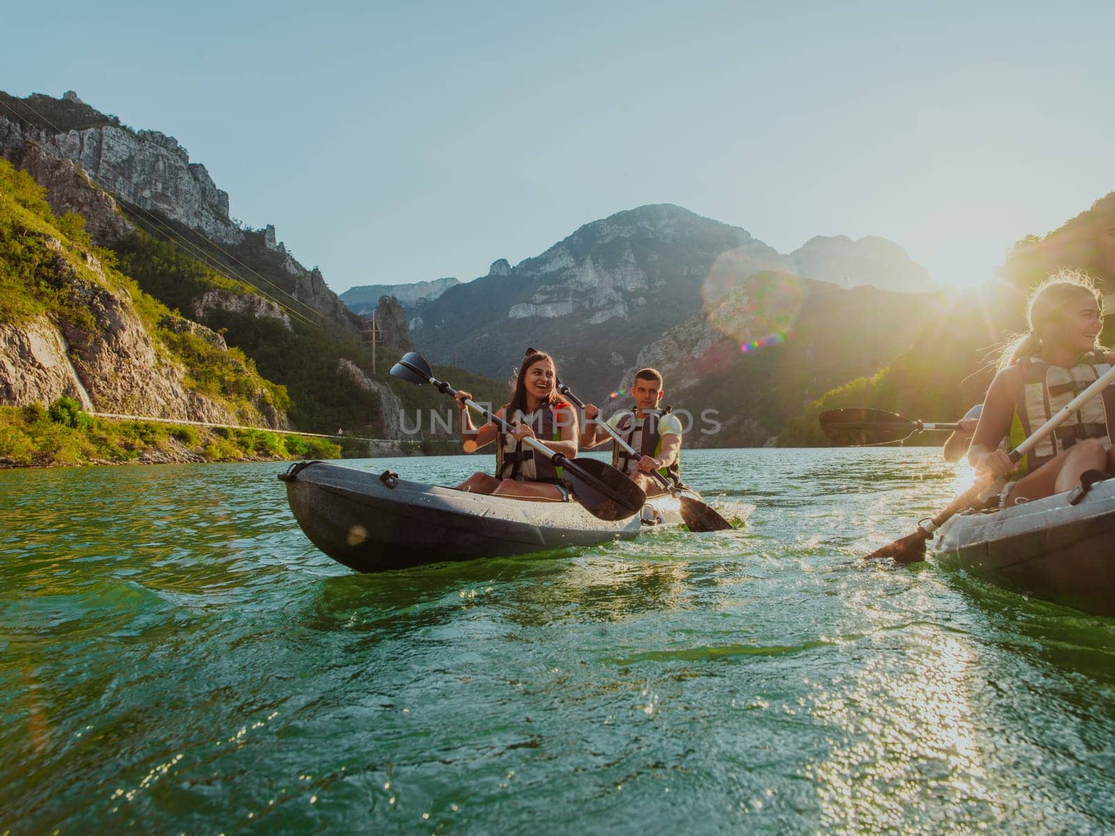 A group of friends enjoying fun and kayaking exploring the calm river, surrounding forest and large natural river canyons during an idyllic sunset