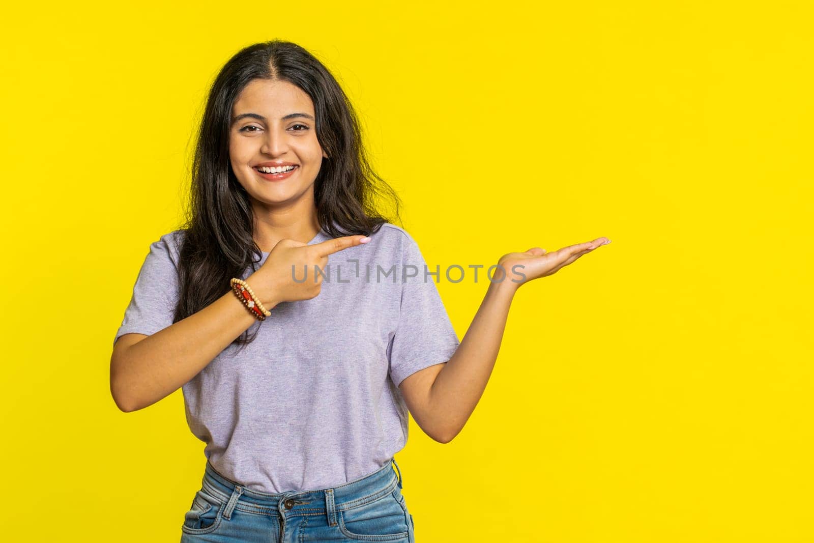 Indian woman showing thumbs up and pointing right empty place, advertising area for commercial text copy space for goods promotion advertisement. Hindu girl isolated on yellow background. Lifestyles