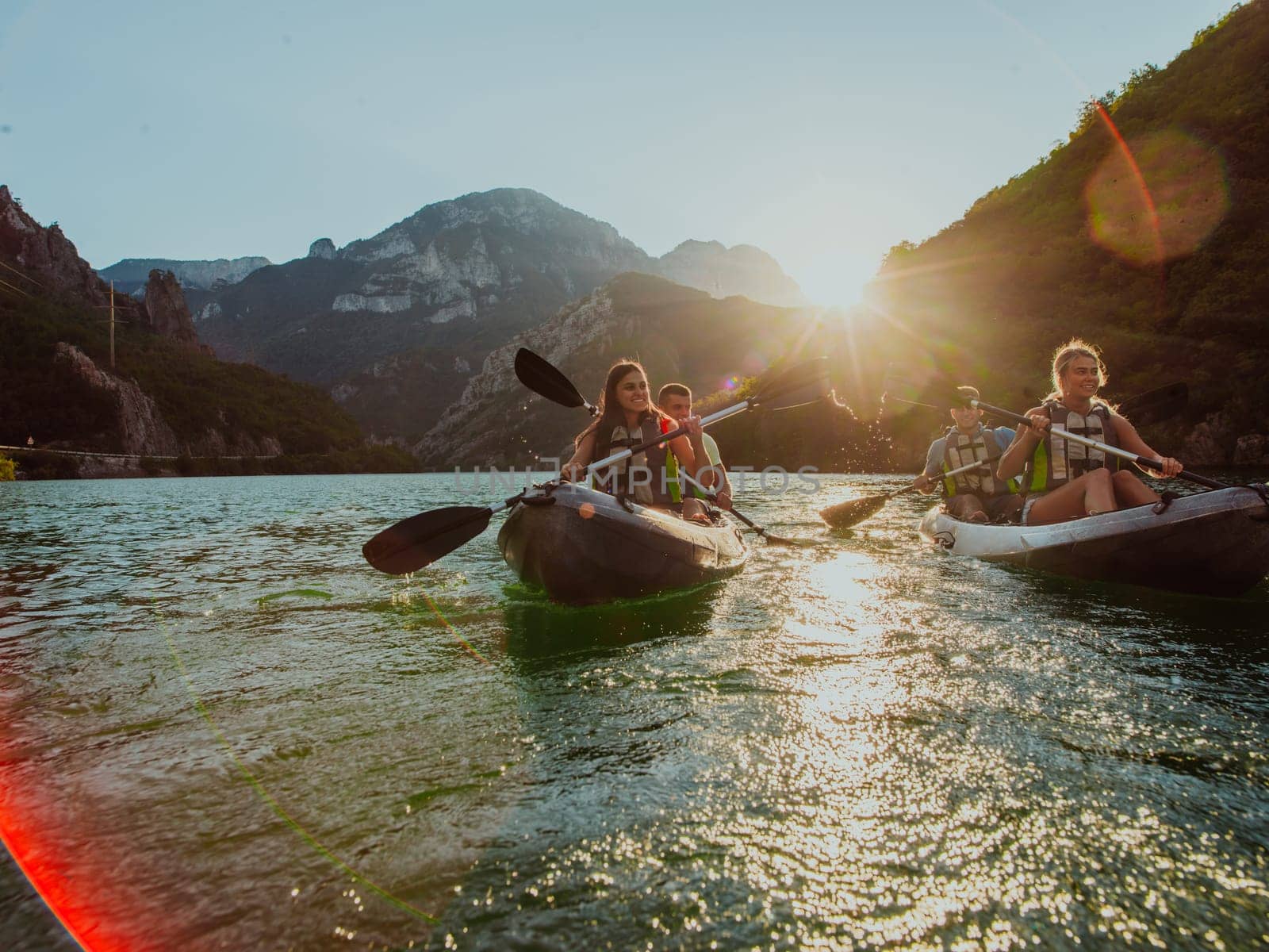 A group of friends enjoying fun and kayaking exploring the calm river, surrounding forest and large natural river canyons during an idyllic sunset