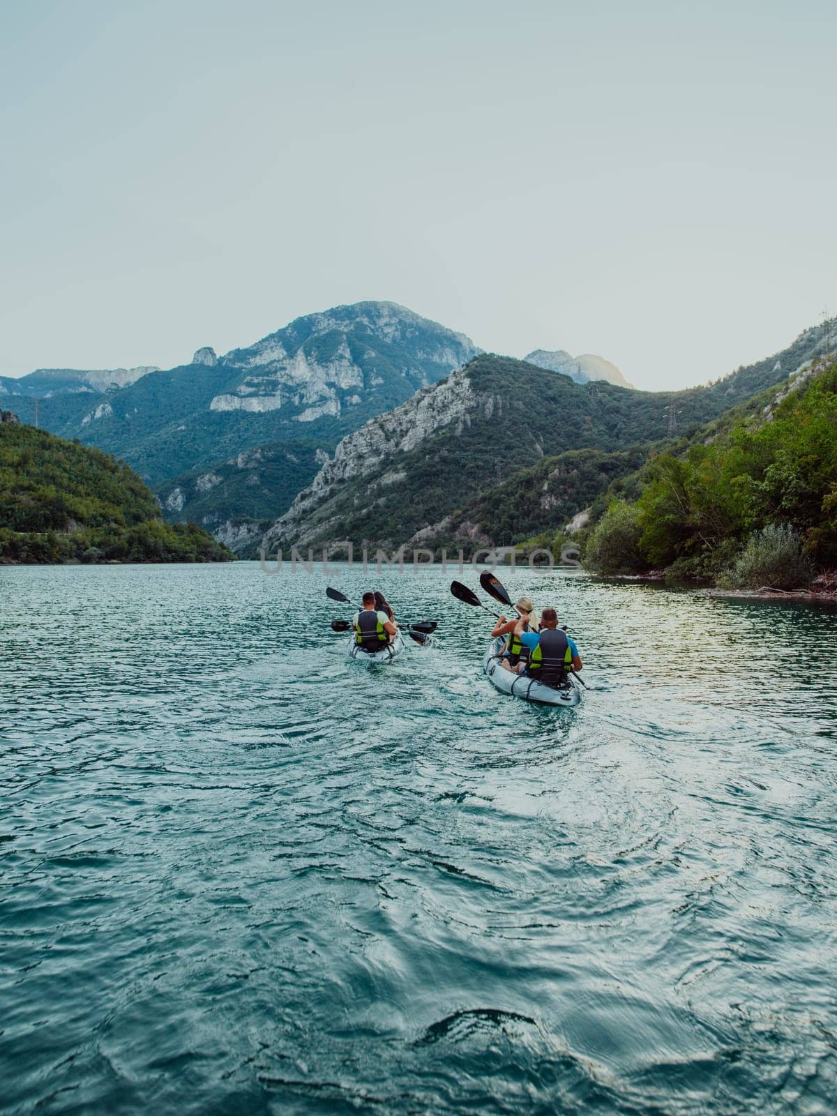 A group of friends enjoying fun and kayaking exploring the calm river, surrounding forest and large natural river canyons during an idyllic sunset. by dotshock