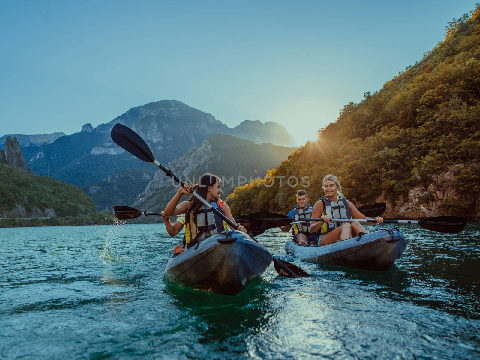 A group of friends enjoying fun and kayaking exploring the calm river, surrounding forest and large natural river canyons during an idyllic sunset