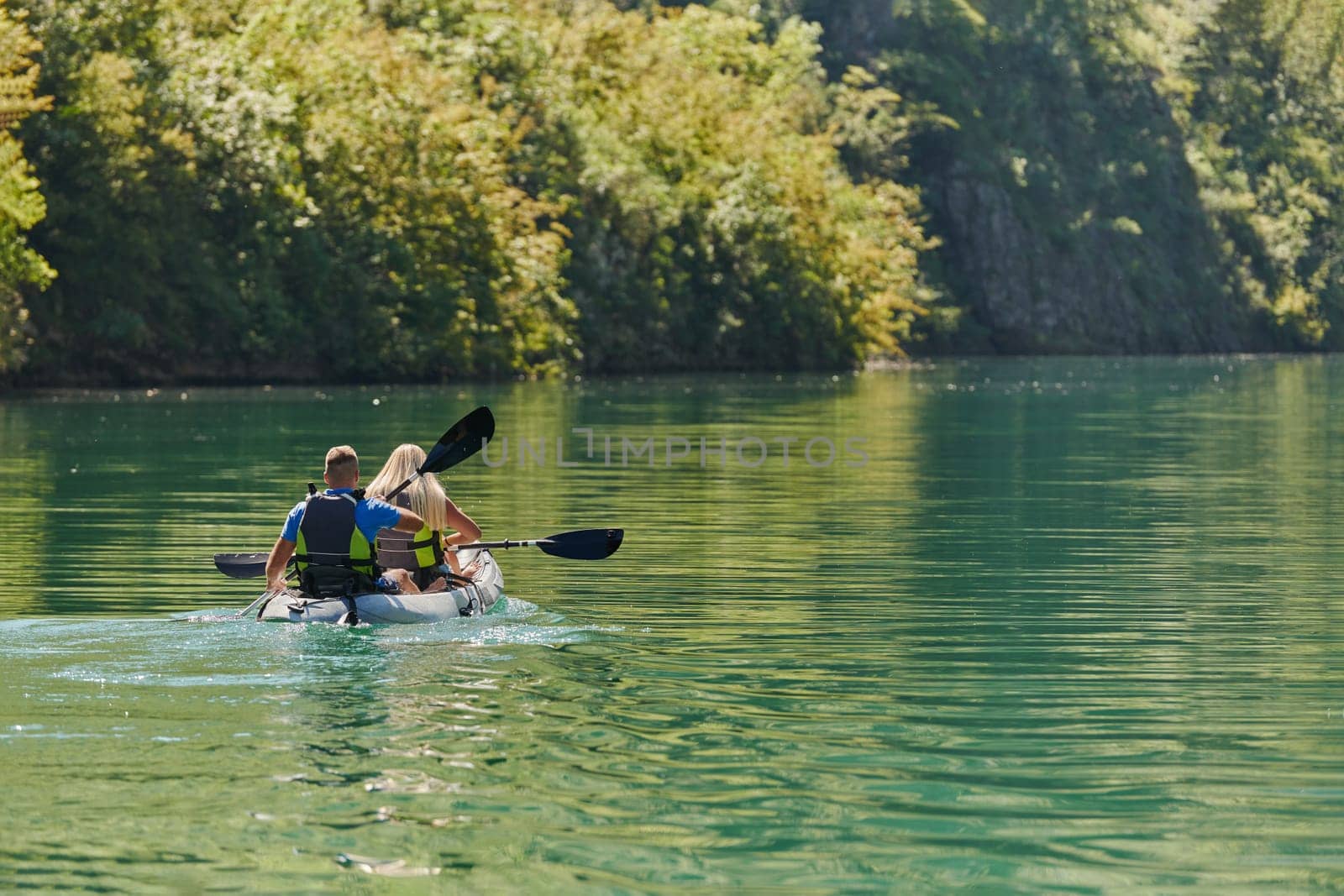 A young couple enjoying an idyllic kayak ride in the middle of a beautiful river surrounded by forest greenery.