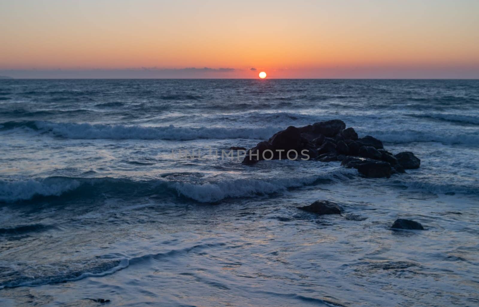 stones in the Mediterranean sea near the beach rocks against the backdrop of sunset