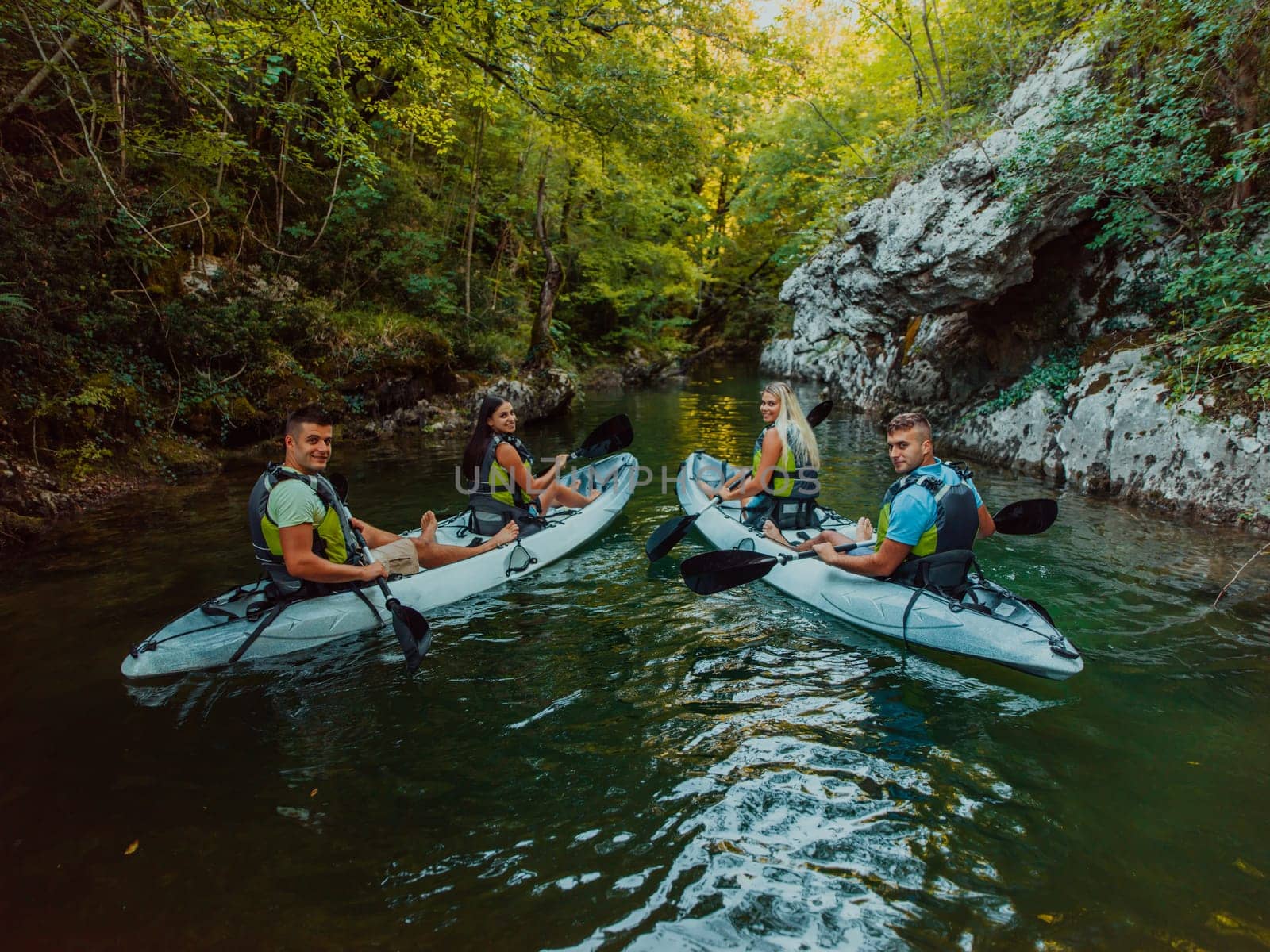 A group of friends enjoying having fun and kayaking while exploring the calm river, surrounding forest and large natural river canyons.