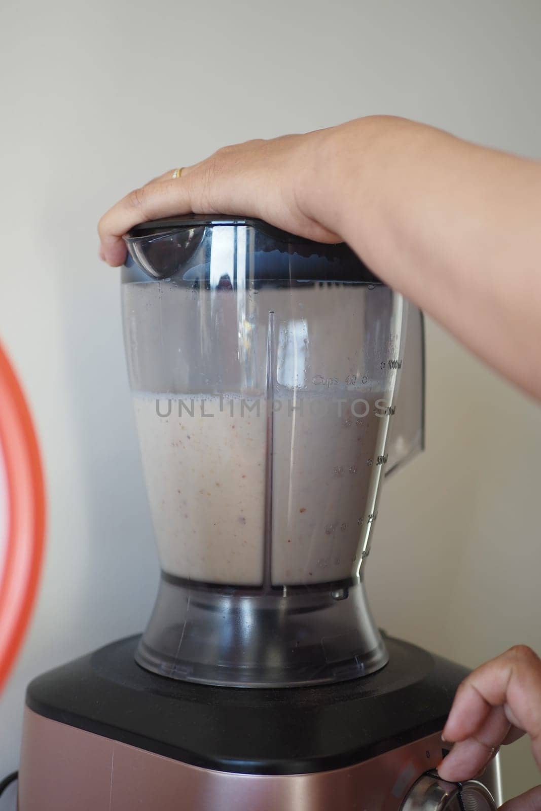 A person is using a kitchen appliance to make a fluid drink. They are blending food, water, and other ingredients to create a smoothie