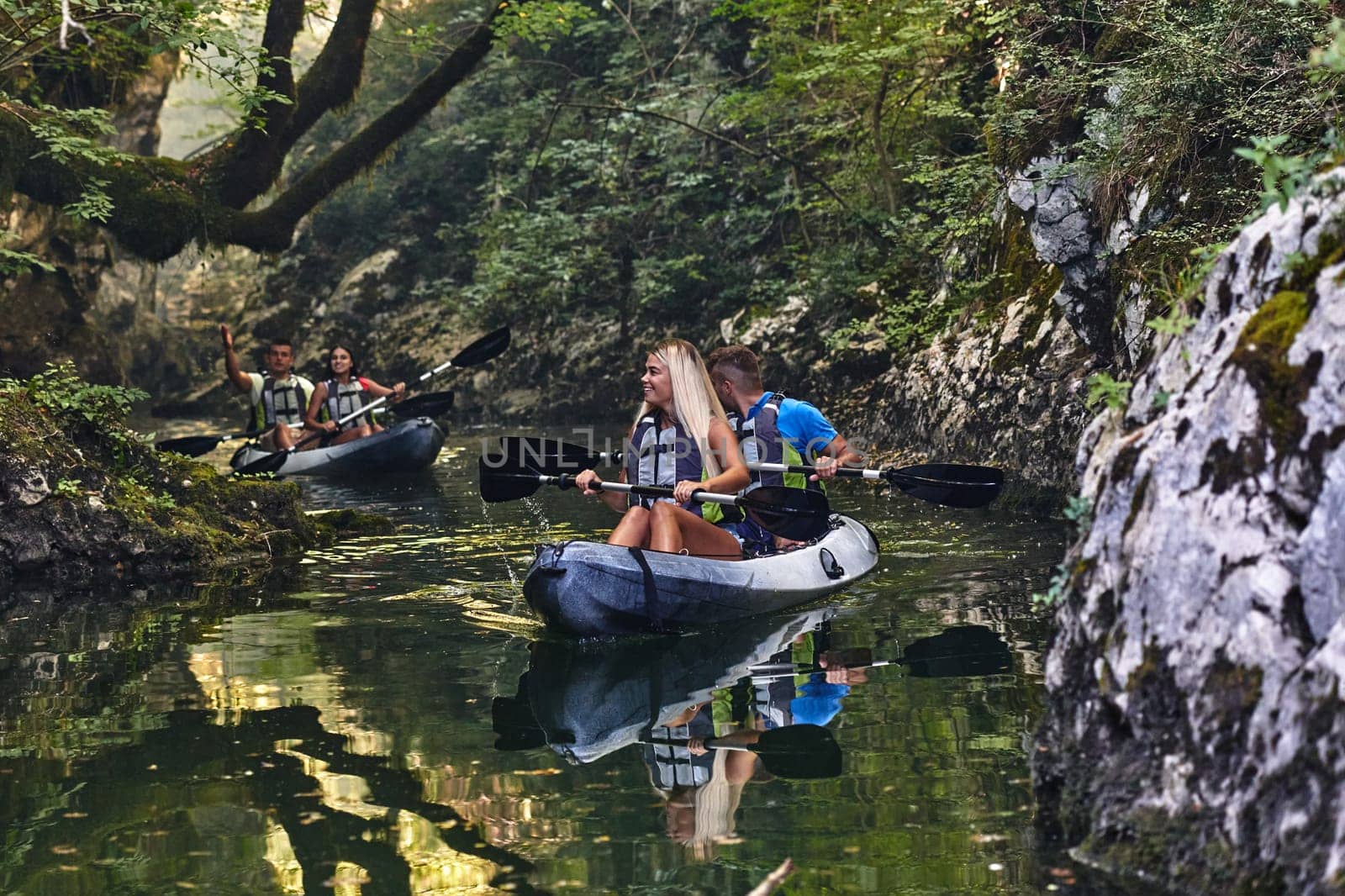 A group of friends enjoying having fun and kayaking while exploring the calm river, surrounding forest and large natural river canyons.