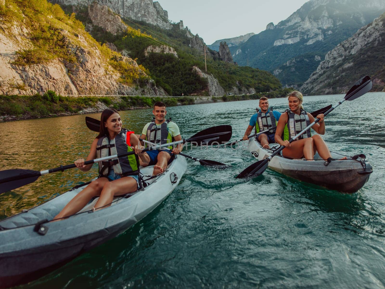 A group of friends enjoying fun and kayaking exploring the calm river, surrounding forest and large natural river canyons during an idyllic sunset