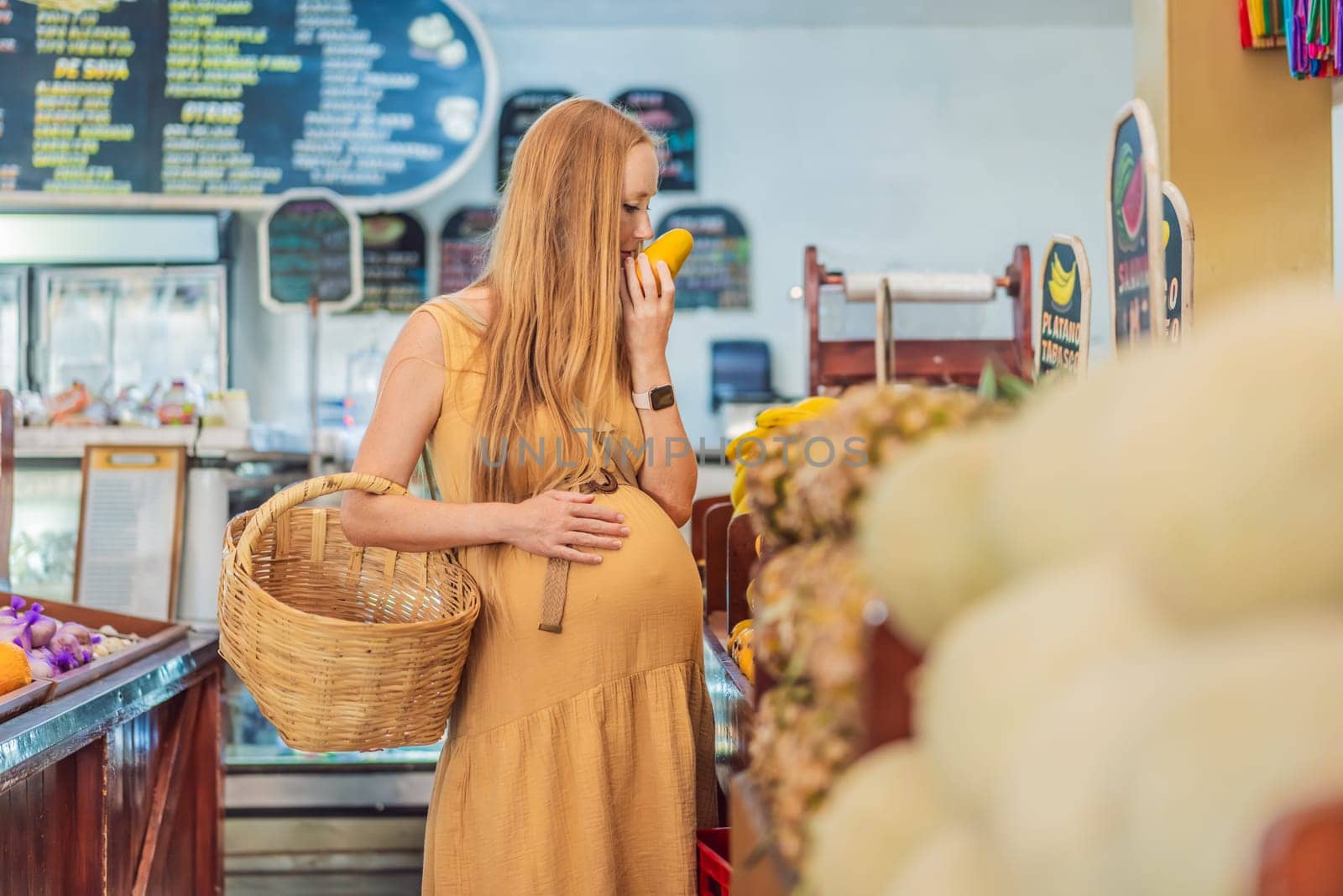 A pregnant woman is at a fruit stand in a grocery store Pregnant woman buying organic vegetables and fruits at Mexican style farmers market by galitskaya