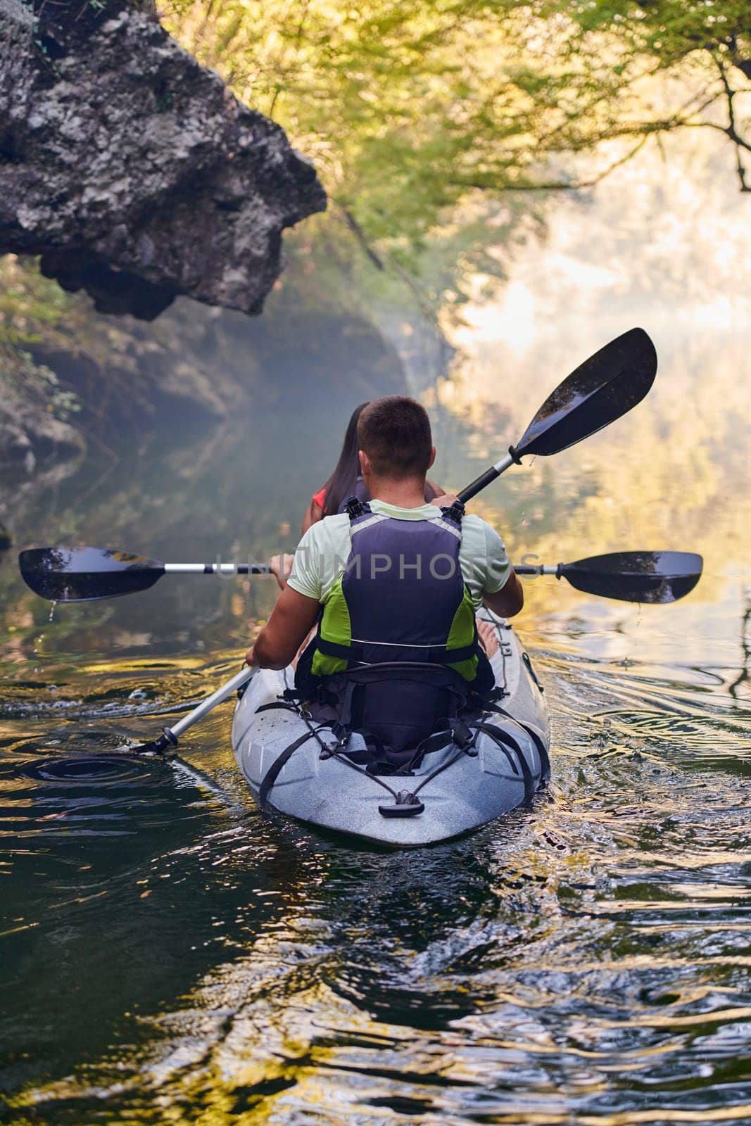 A young couple enjoying an idyllic kayak ride in the middle of a beautiful river surrounded by forest greenery by dotshock