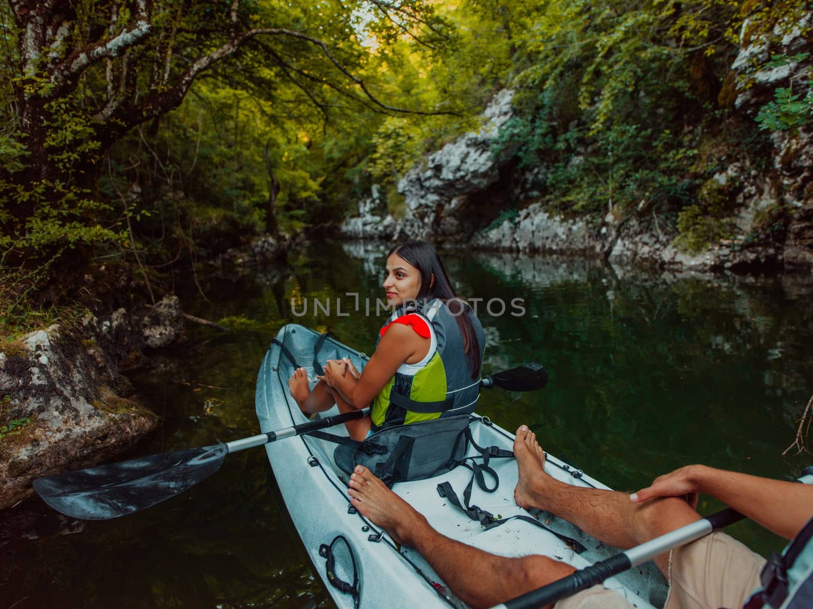 A young couple enjoying an idyllic kayak ride in the middle of a beautiful river surrounded by forest greenery.