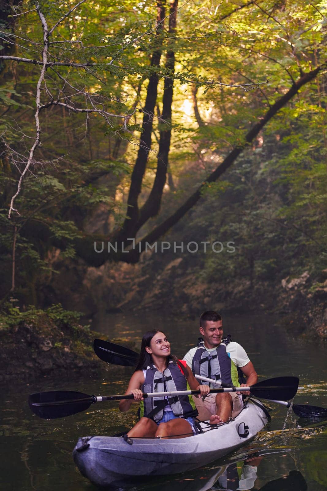 A young couple enjoying an idyllic kayak ride in the middle of a beautiful river surrounded by forest greenery.