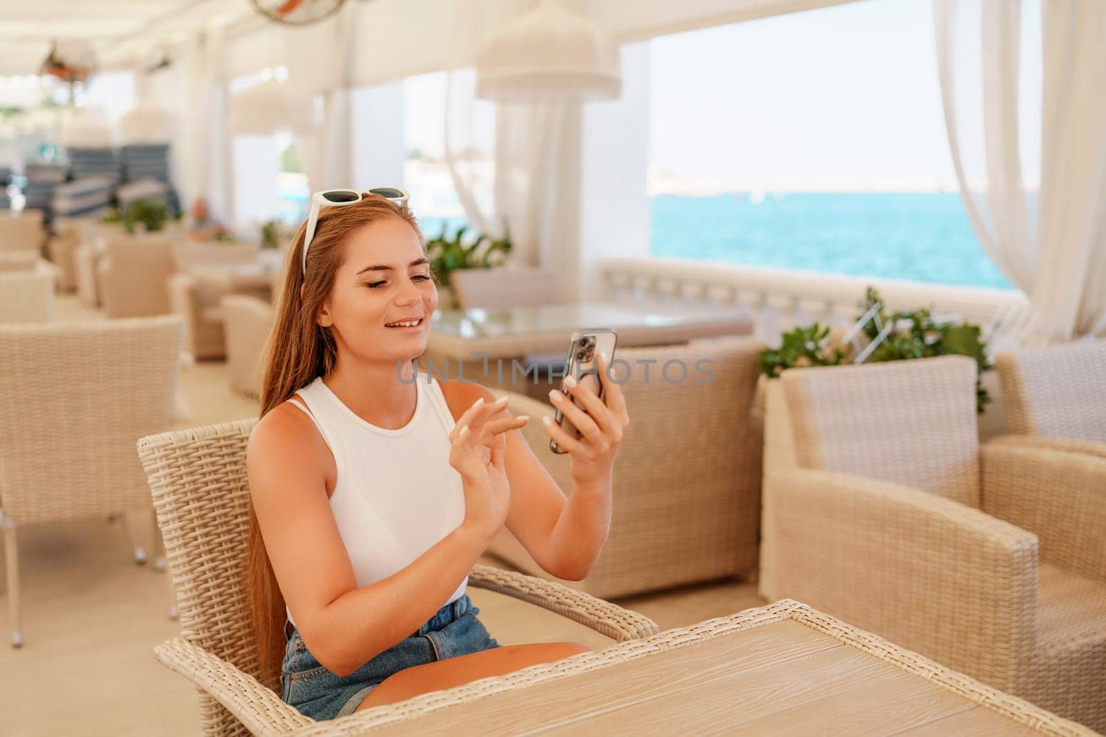 A woman is sitting at a table with a cell phone in her hand. She is taking a picture of the ocean