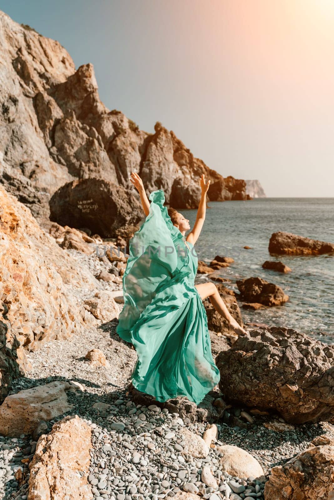 Woman green dress sea. Woman in a long mint dress posing on a beach with rocks on sunny day. Girl on the nature on blue sky background