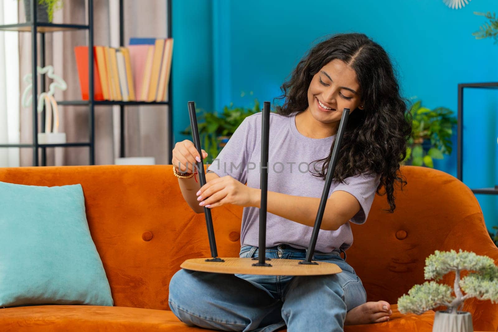 Happy Indian young woman finishing assembling furniture at home. Successful table desk collect repair fixing. Arabian girl after moving into new apartment. Advertisement of a furniture store. Mortgage