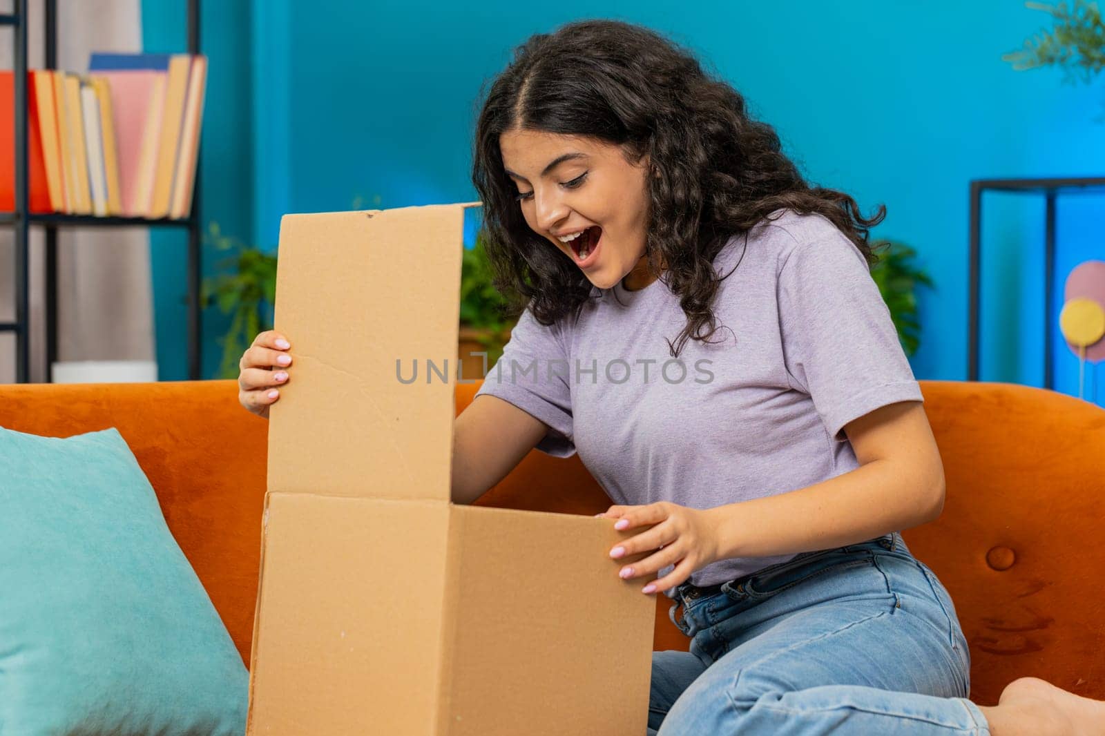 Happy Indian young woman unpacking delivery parcel sits at home. Smiling satisfied Arabian Hindu girl shopper online shop customer opening cardboard box receive purchase gift by fast postal shipping