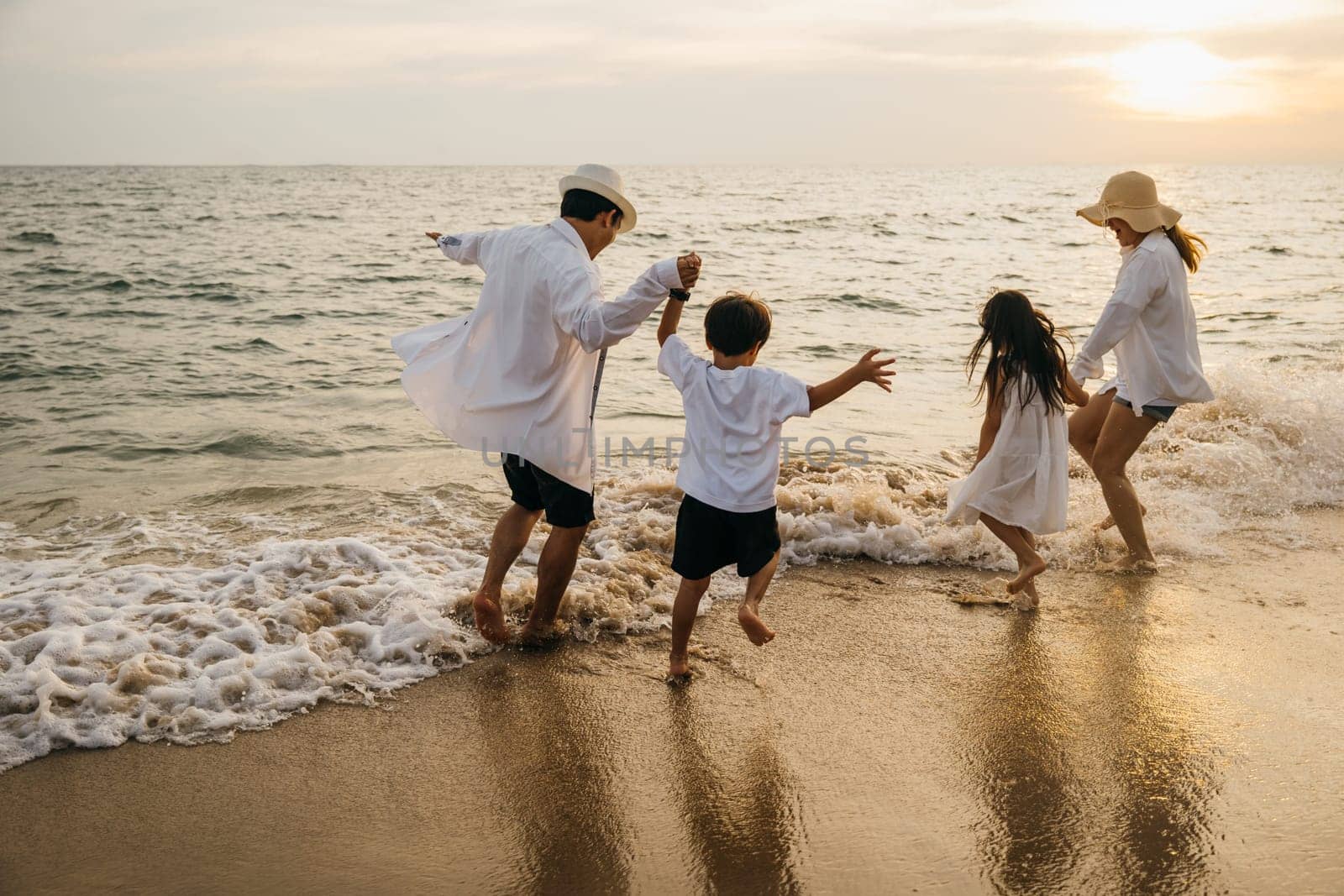 A joyful Asian family back view enjoys quality time on beach. Parents and daughters bond playing and pretending to fly with arms outstretched. carefree and happy weekend moment captured under sun.