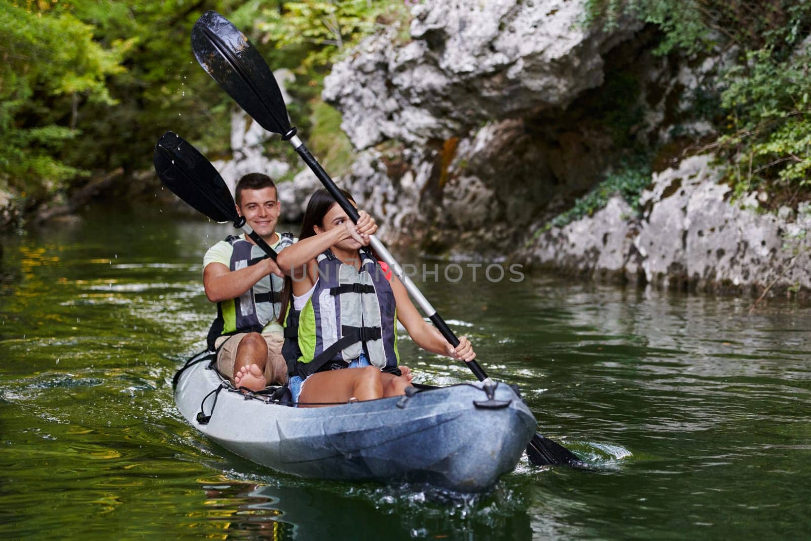 A young couple enjoying an idyllic kayak ride in the middle of a beautiful river surrounded by forest greenery.