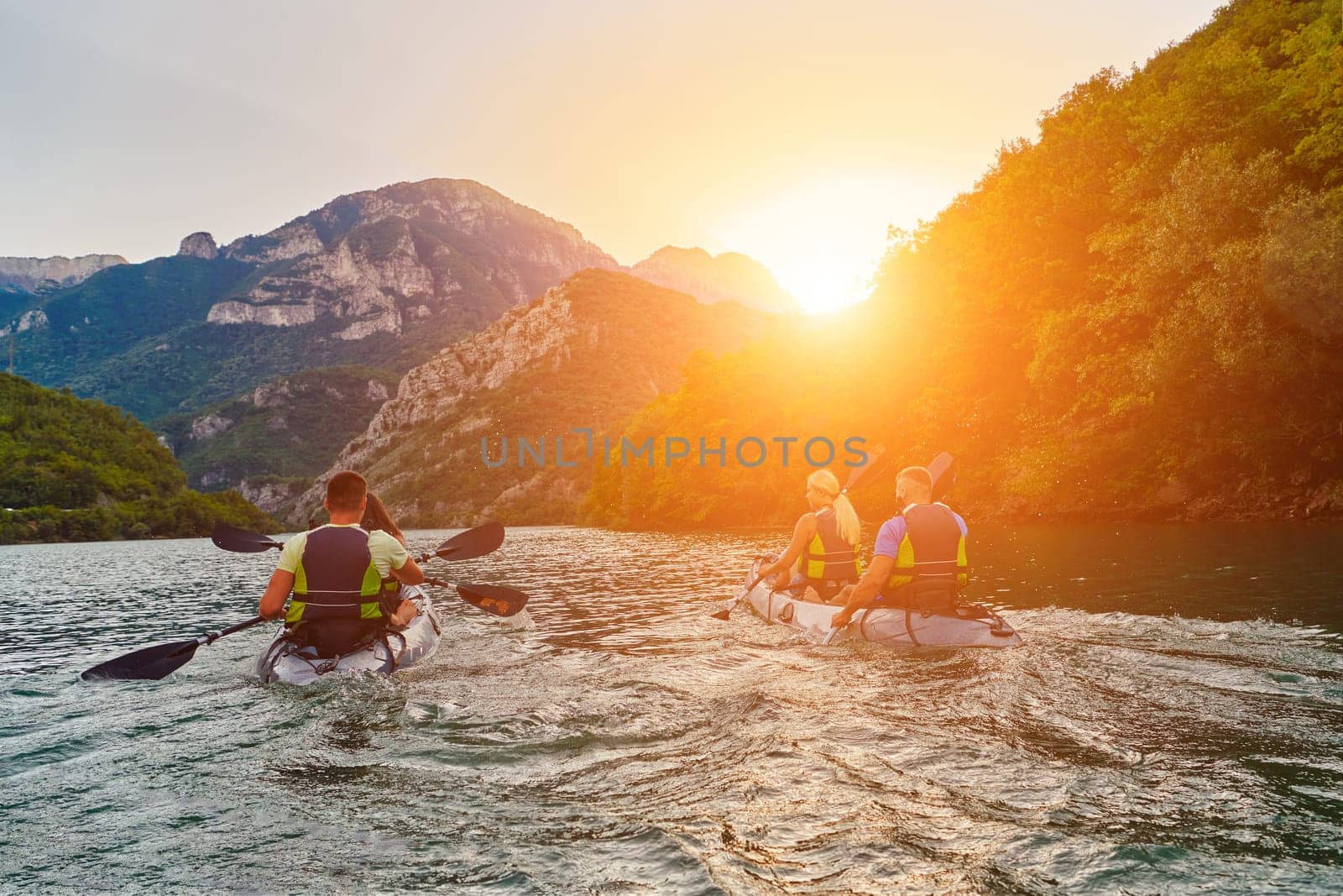 A group of friends enjoying fun and kayaking exploring the calm river, surrounding forest and large natural river canyons during an idyllic sunset