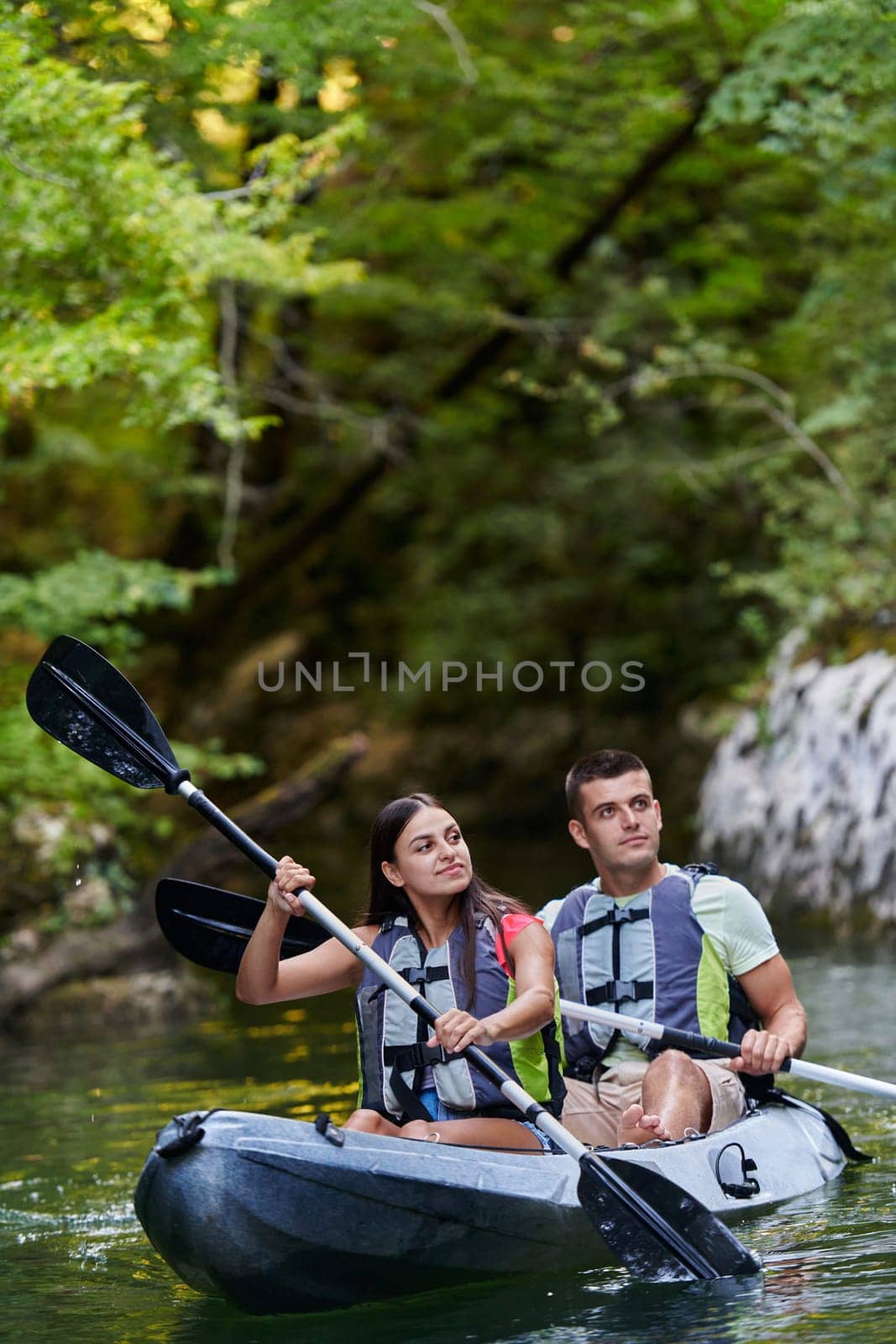 A young couple enjoying an idyllic kayak ride in the middle of a beautiful river surrounded by forest greenery by dotshock