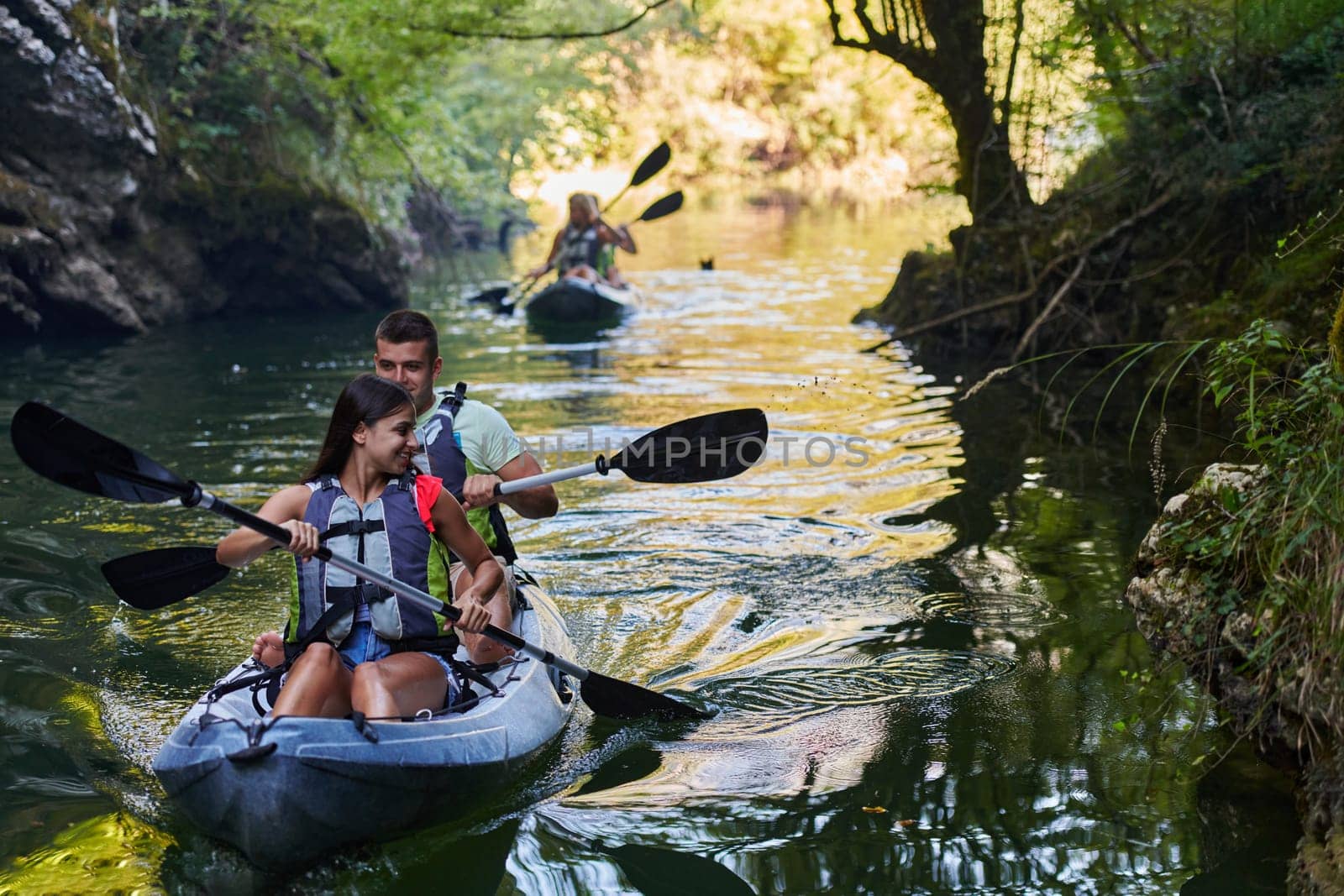 A group of friends enjoying having fun and kayaking while exploring the calm river, surrounding forest and large natural river canyons.