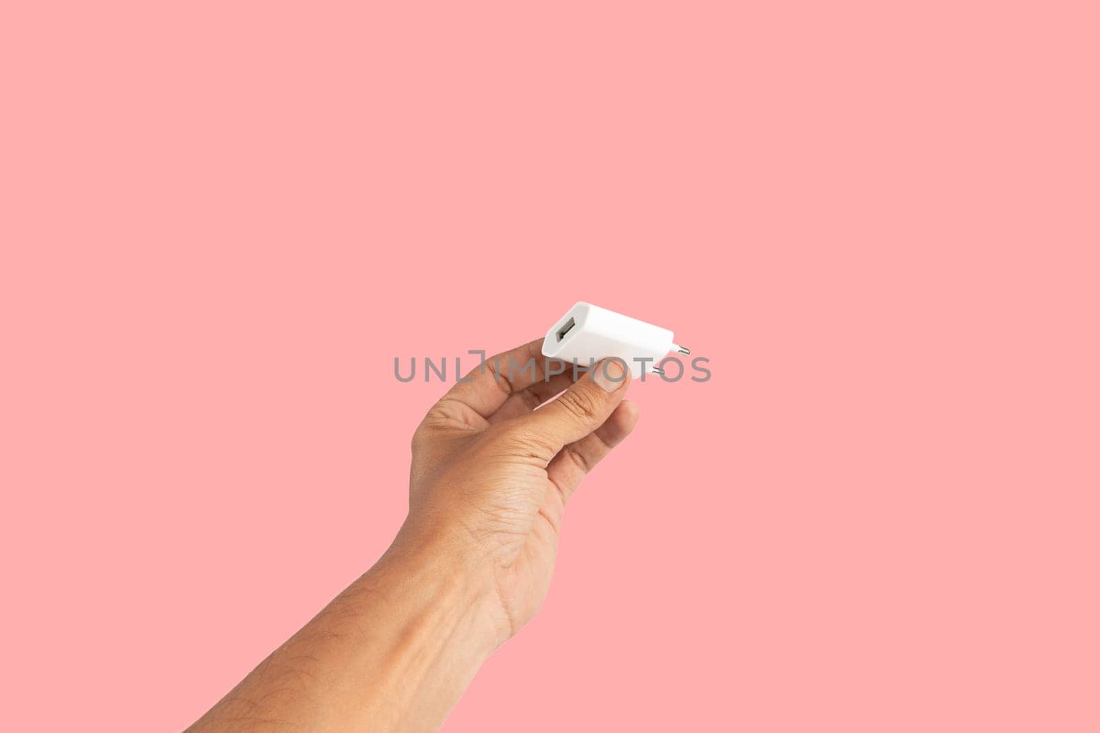 Black male hand holding a USB charger plug isolated on pink background. High quality photo