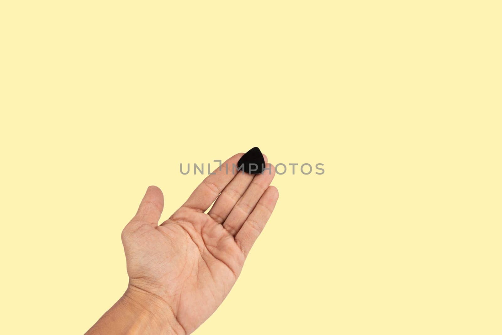 Black male hand holding a guitar pick isolated on light yellow background. High quality photo