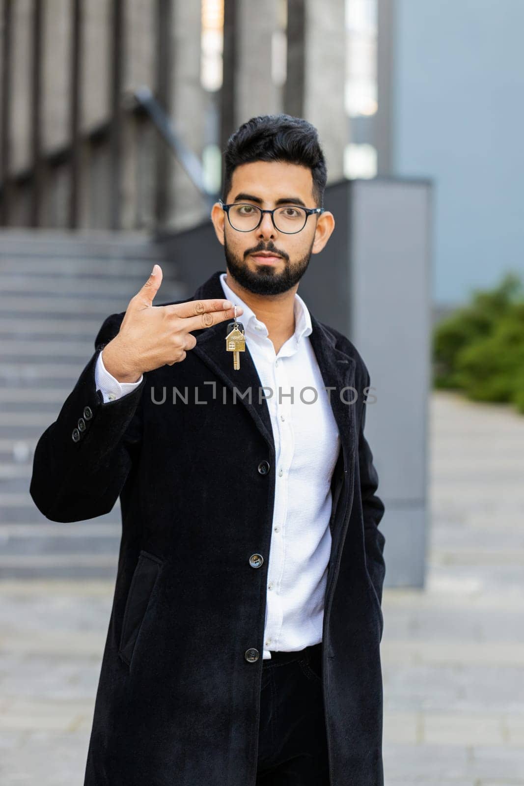 Indian businessman real estate agent lifting hand showing keys of new home house apartment buying or renting property, mortgage loan, investment outdoors. Arabian Hindu freelancer guy in downtown city