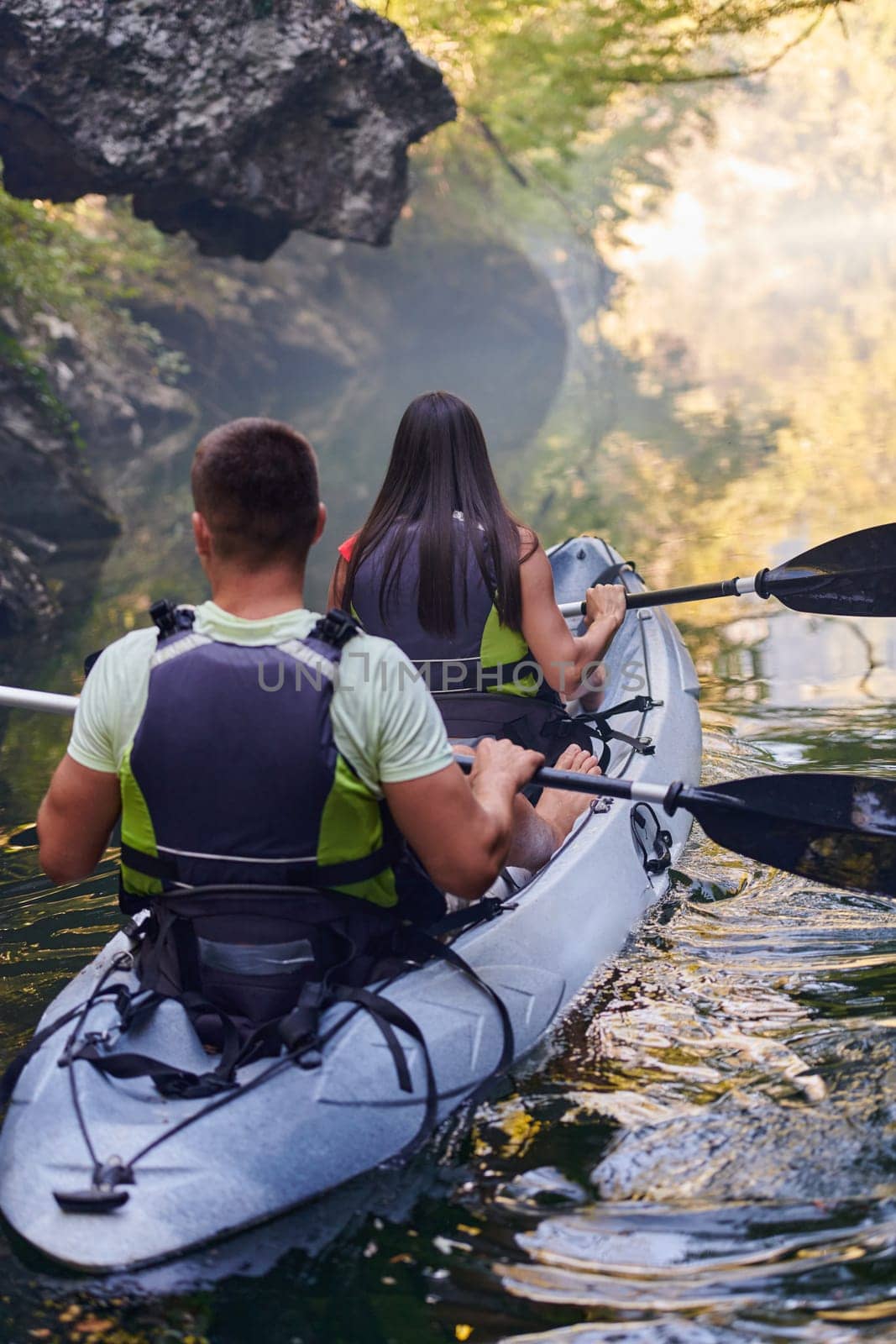 A young couple enjoying an idyllic kayak ride in the middle of a beautiful river surrounded by forest greenery.