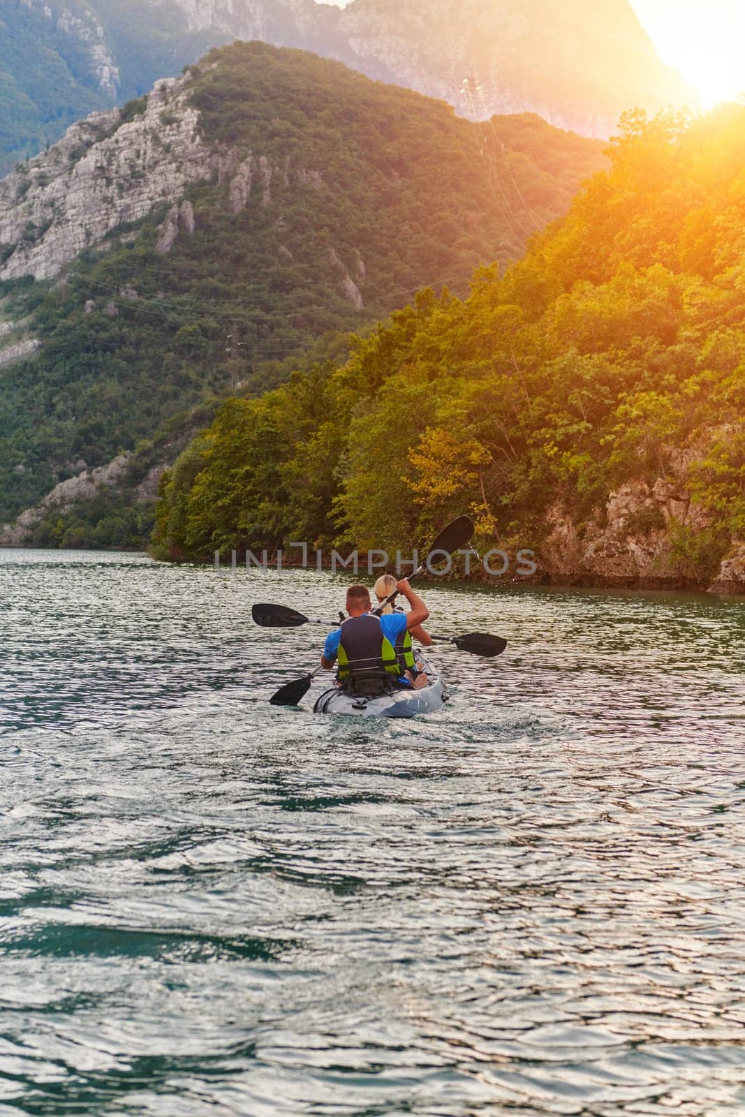 A young couple enjoying an idyllic kayak ride in the middle of a beautiful river surrounded by forest greenery in sunset time by dotshock