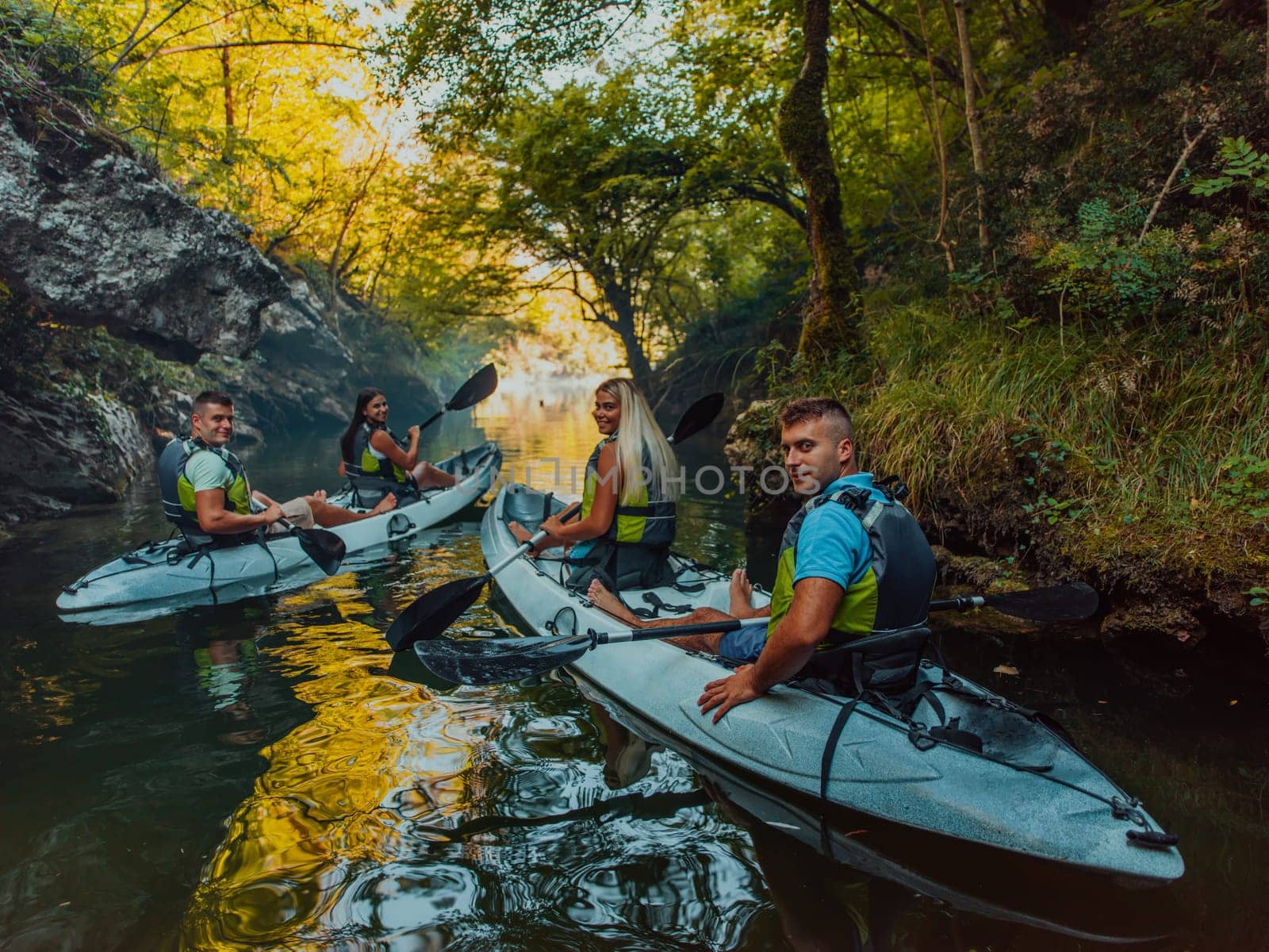 A group of friends enjoying having fun and kayaking while exploring the calm river, surrounding forest and large natural river canyons.