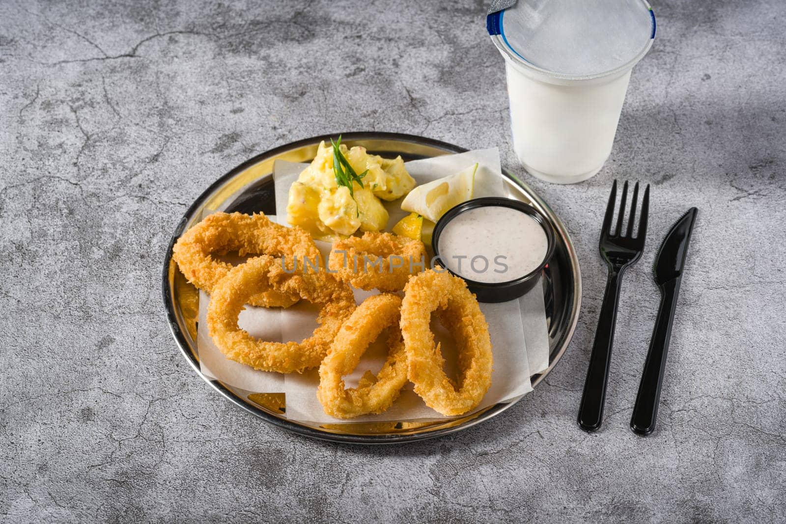 Fried calamari with potato salad next to it on stone table by Sonat