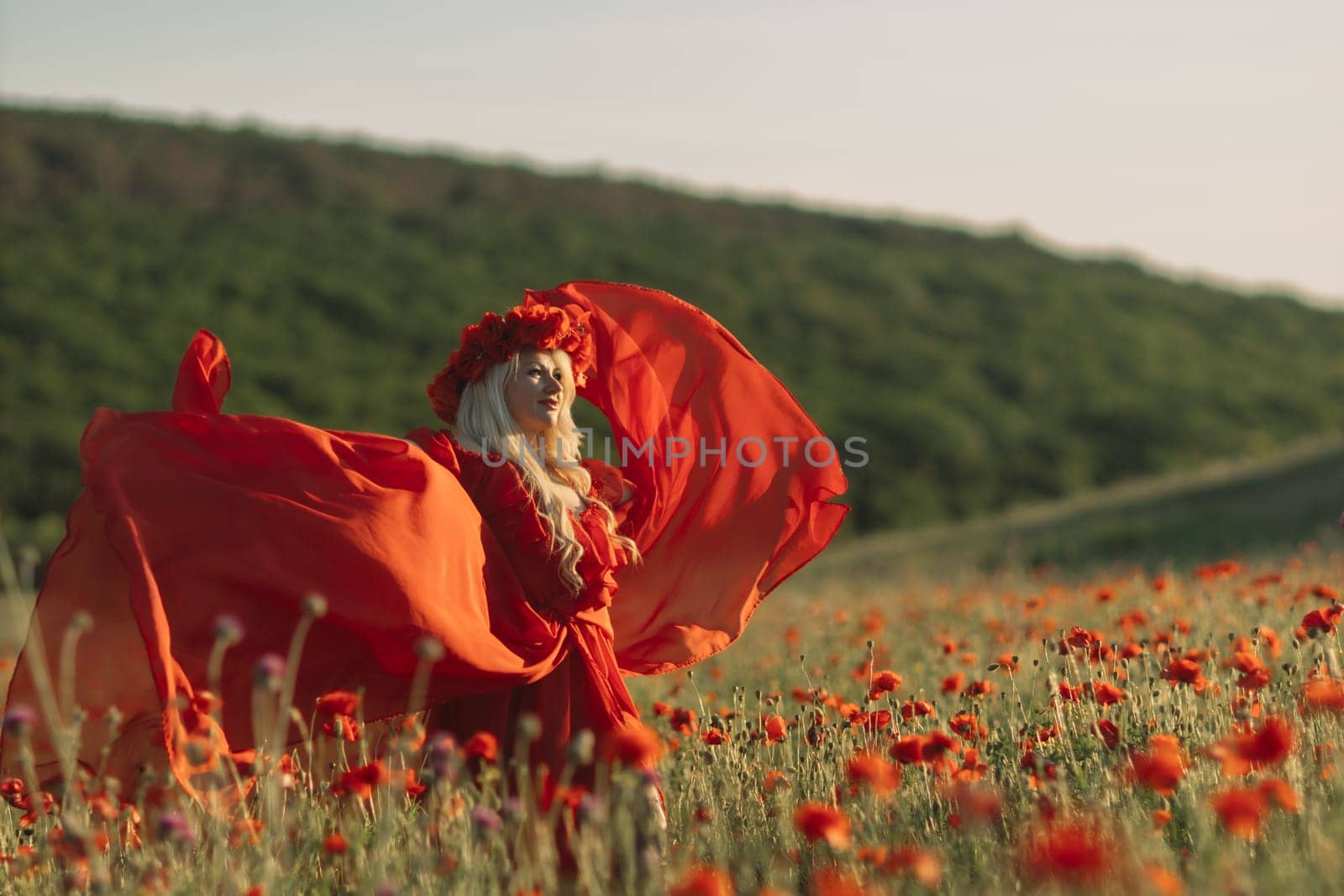 A woman in a red dress is standing in a field of red flowers. The scene is serene and peaceful, with the woman's flowing dress and the vibrant red flowers creating a sense of beauty and tranquility