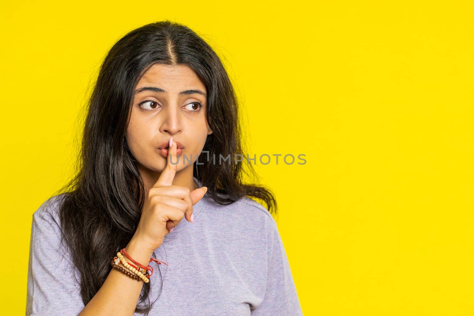Shh be quiet please. Indian young woman presses index finger to lips makes silence gesture sign do not tells secret, stop talk gossip, confidential privacy. Arabian girl isolated on yellow background