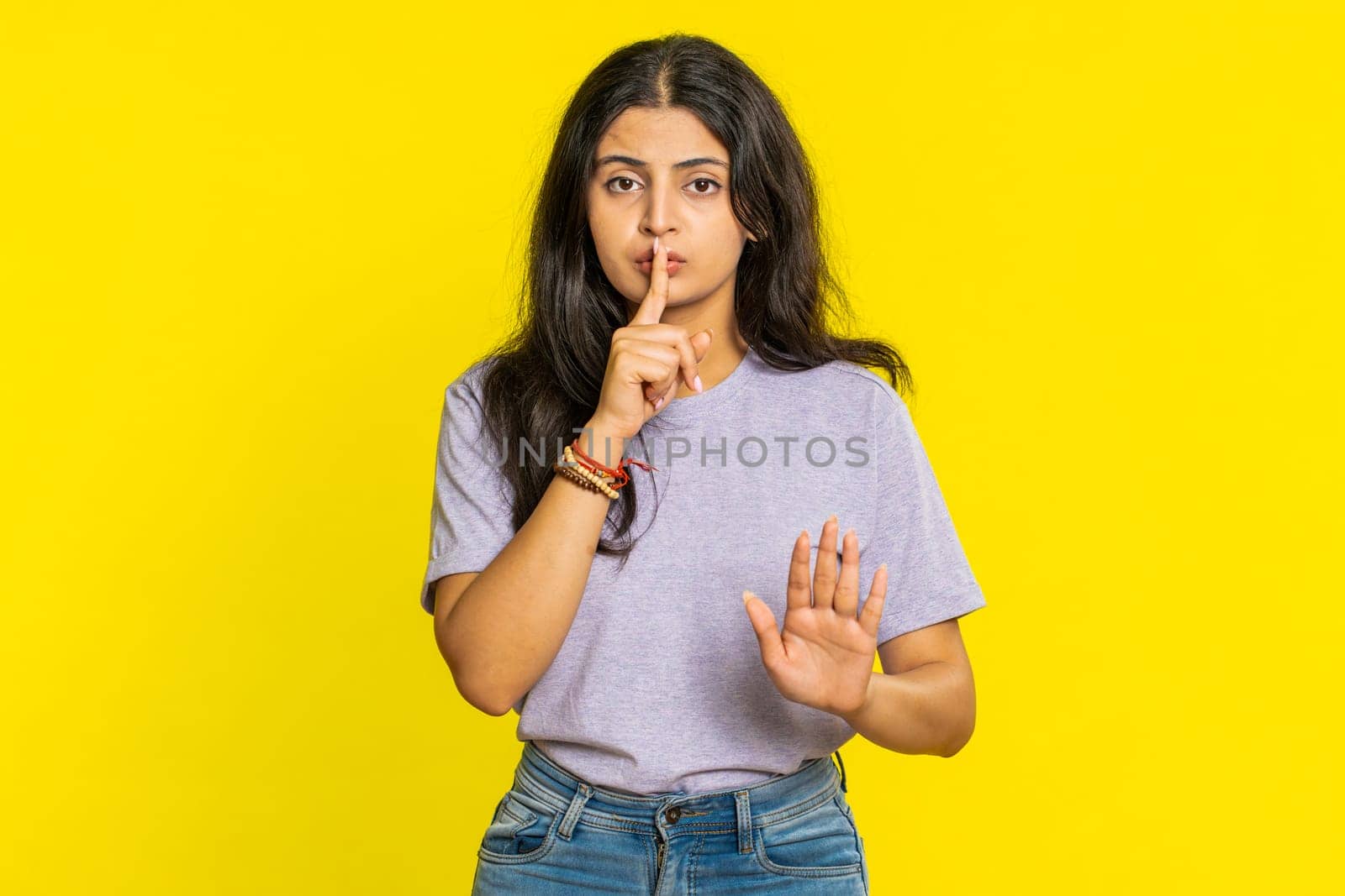 Shh be quiet please. Indian young woman presses index finger to lips makes silence gesture sign do not tells secret, stop talk gossip, confidential privacy. Arabian girl isolated on yellow background