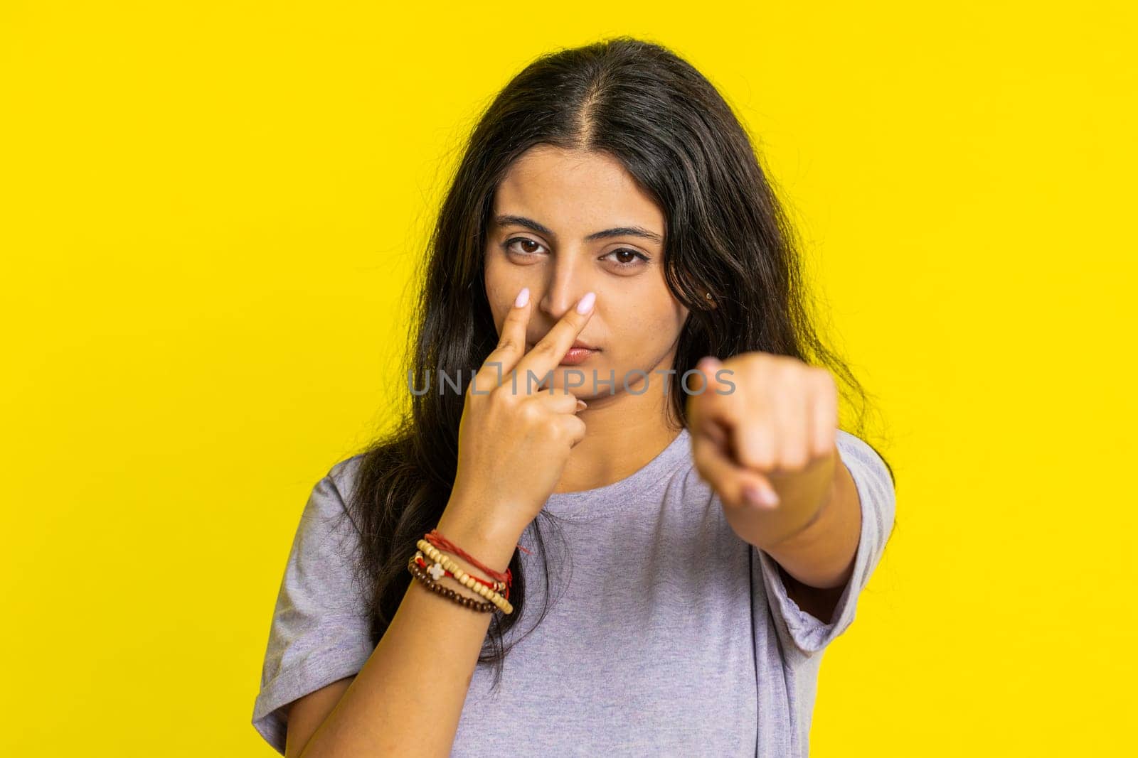 I am watching you. Confident attentive woman pointing at her eyes and camera, show I am watching you gesture spying on someone. Pretty disappointed Indian girl isolated on yellow studio background