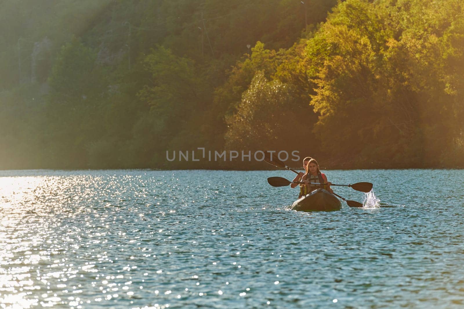 A young couple enjoying an idyllic kayak ride in the middle of a beautiful river surrounded by forest greenery in sunset time by dotshock