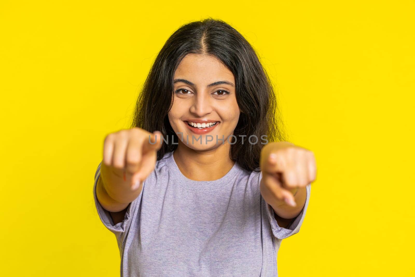 I choose you. Indian smiling woman pointing finger to camera and looking with playful happy expression, making winner choice, showing direction. Arabian young girl isolated on yellow studio background