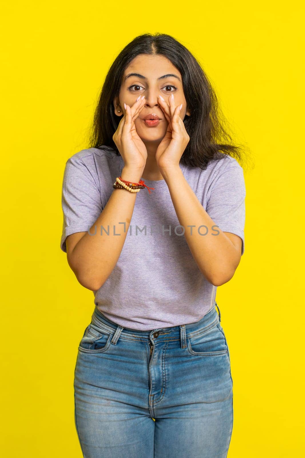 Keep my secrets, silence. Indian woman whisper news rumors holding hands near mouth share gossip quiet. Arabian girl telling interesting confidential story isolated on yellow background. Vertical